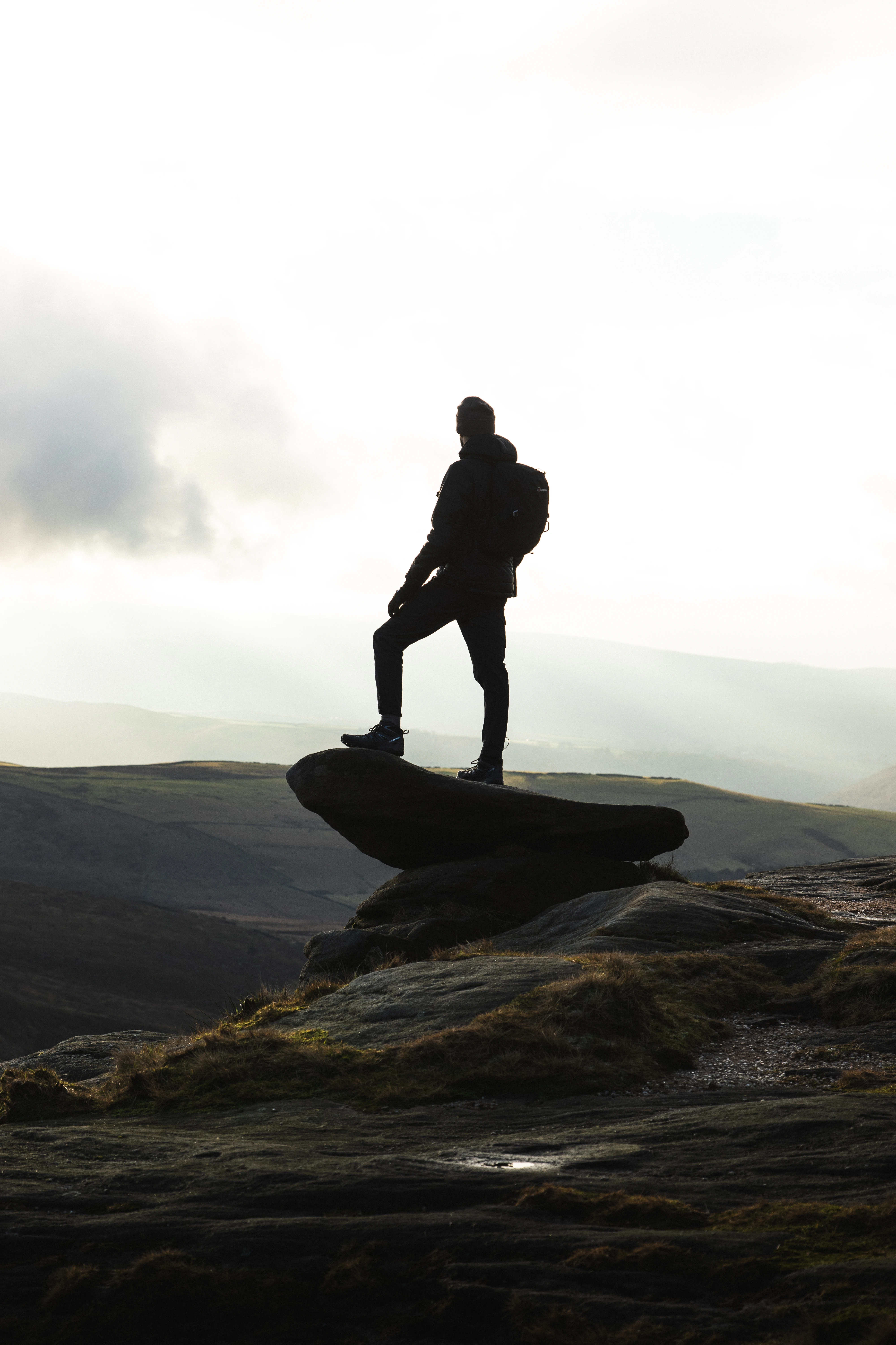 Silhouette of a hiker standing on a rock overlooking moorland hills